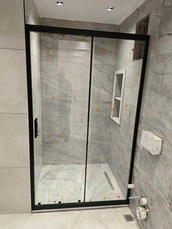 İnce siyah profilli sürgülü duş kapısı, gri mermer seramikli banyo